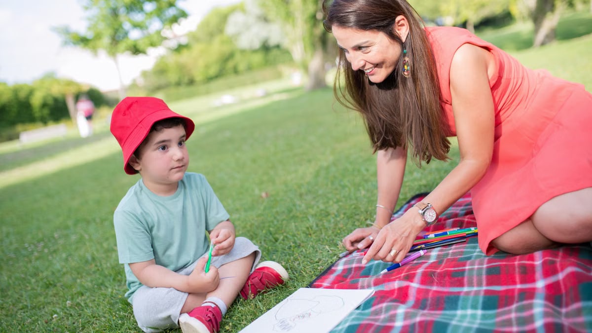 A happy moment between a mother and child drawing outdoors on a picnic blanket.