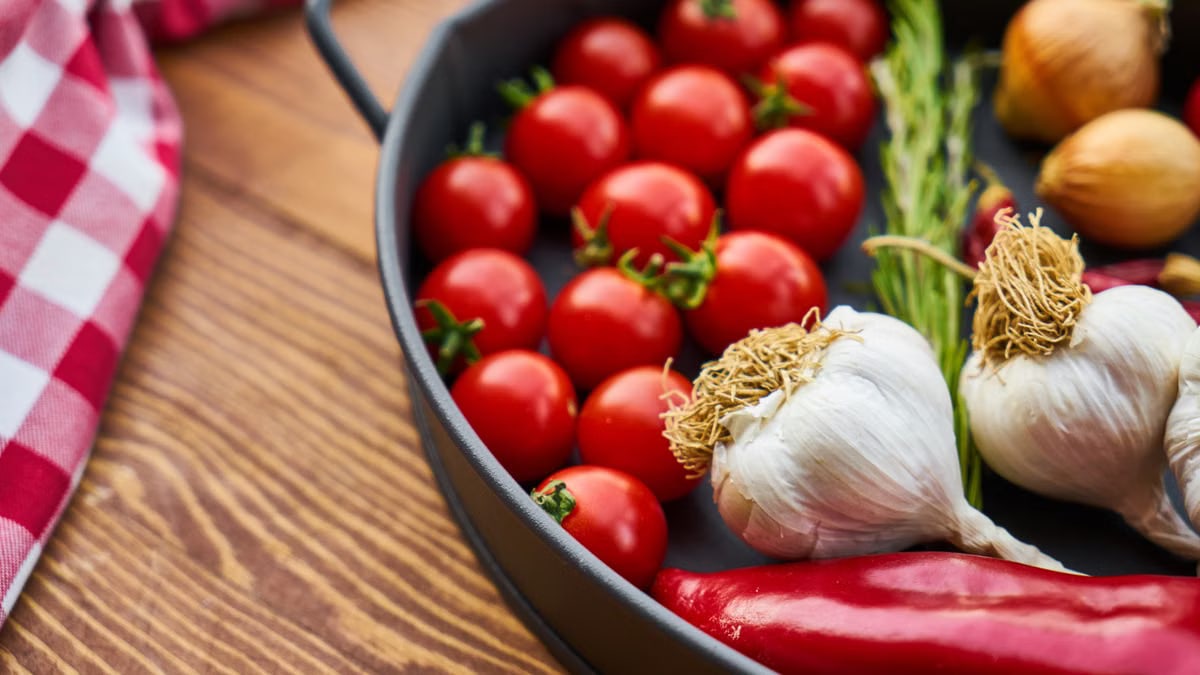 A vivid display of fresh Mediterranean vegetables on a wooden table with a pan.